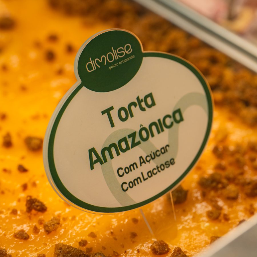 Cuba de gelato Torta Amazônica na vitrine da Dimolise, base alaranjada com crumble e a placa do sabor